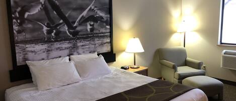 Habitación de hotel con cama, una silla, una lámpara y un cuadro grande en la pared.