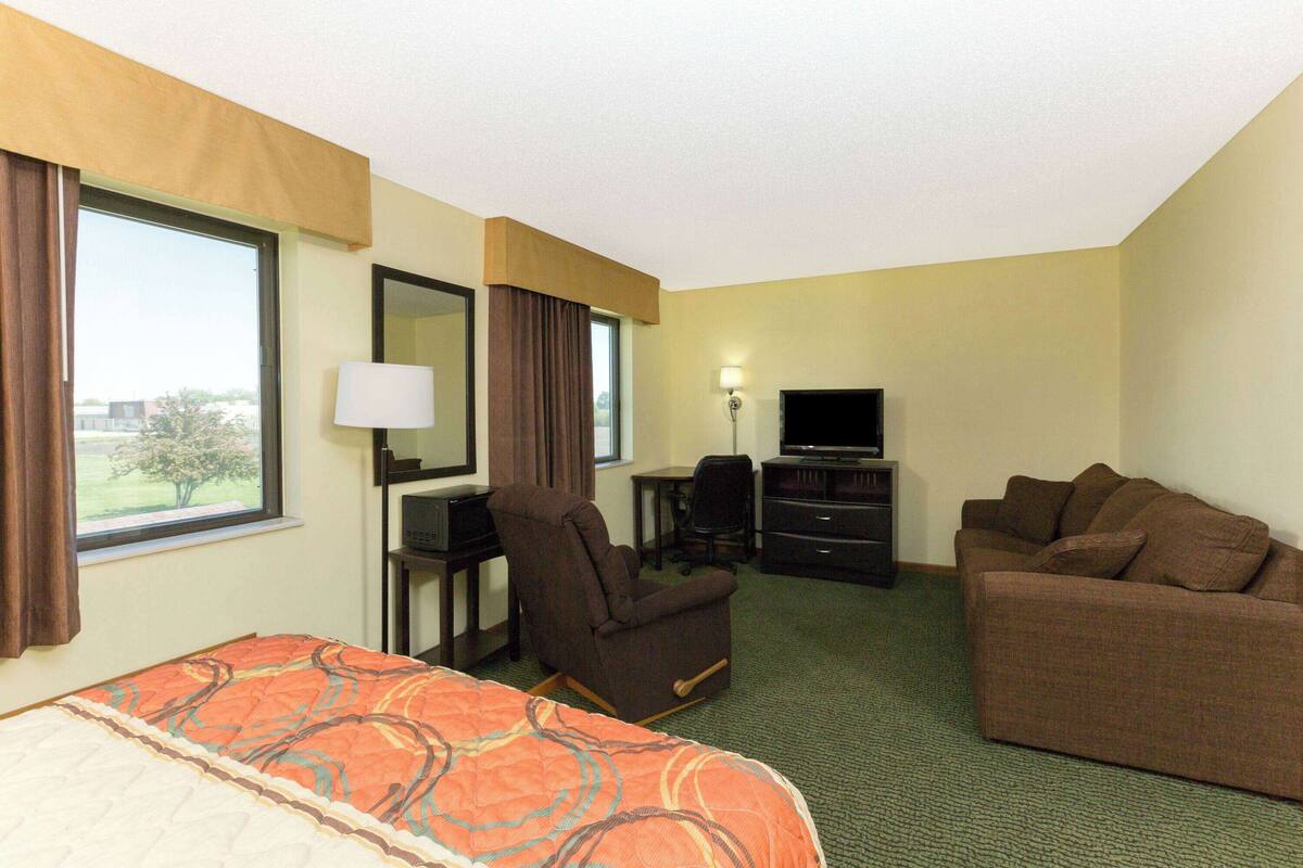 A hotel room with a bed, a sofa, a desk with a chair, a television, and a window with curtains.