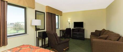 A hotel room with a bed, a sofa, a desk with a chair, a television, and a window with curtains.