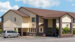 A two-story building with a beige exterior and brown roof, featuring a covered entrance area with brick pillars. - Super 8 by Wyndham Perry IA (Perry)