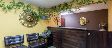 Un área de recepción con un escritorio de madera, dos sillones de cuero, un adorno tipo sol en la pared y un letrero que dice "Super 8".