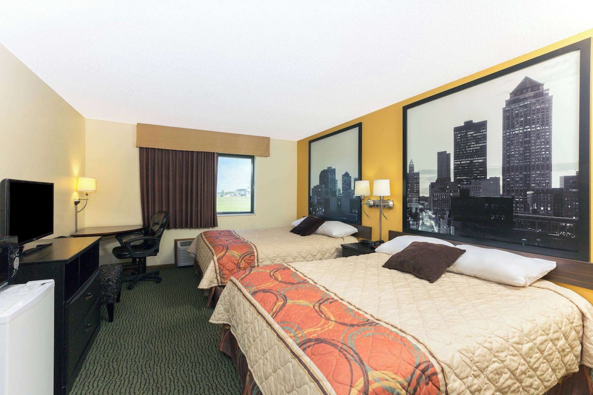 A hotel room with two beds, a desk, a television, and a large cityscape view.