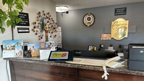 A hotel reception desk with a digital display, a clock, and a sign indicating check-in and check-out times. - Super 8 by Wyndham Perry IA (Perry)
