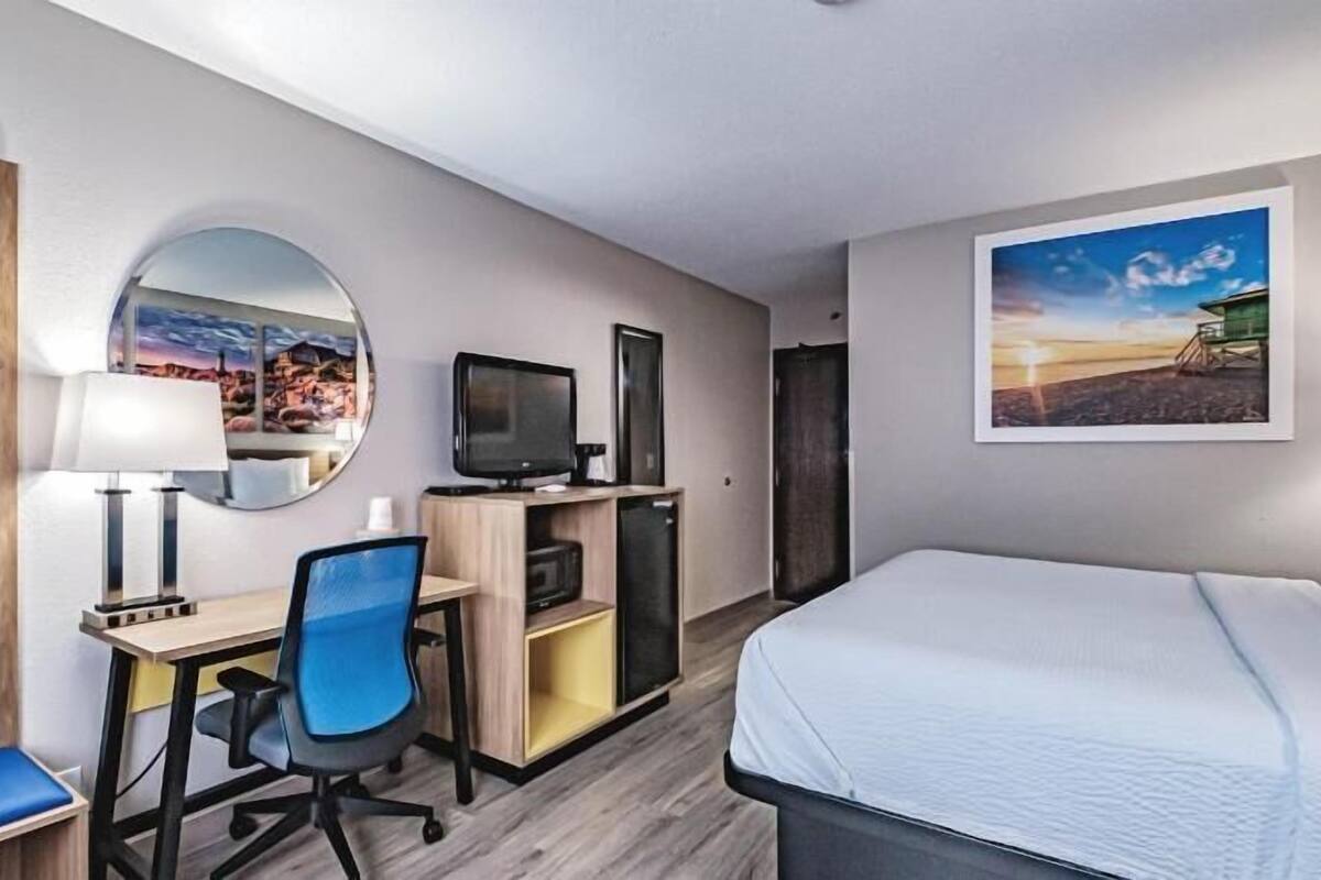 A hotel room with a bed, desk, chair, TV, and a painting on the wall.