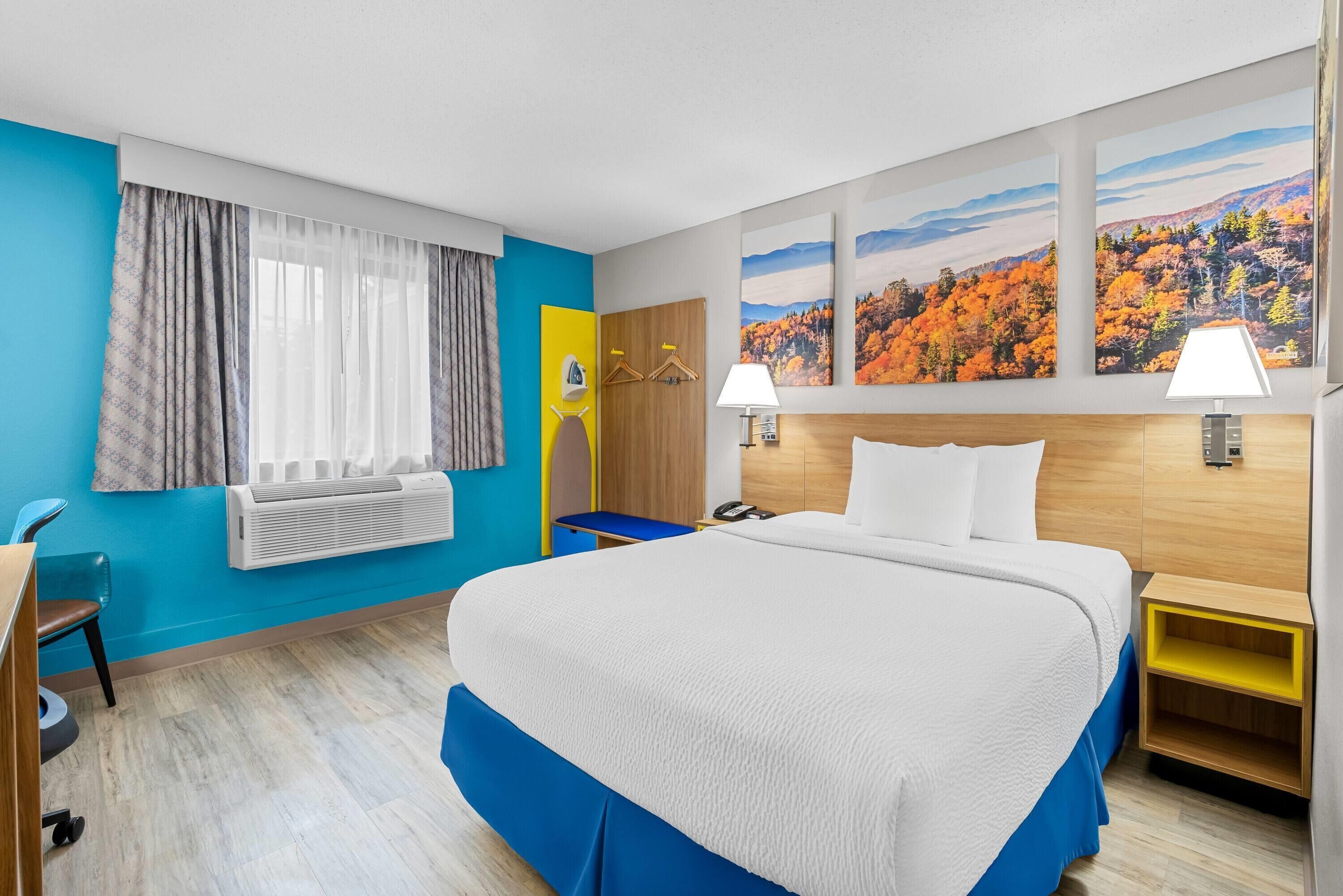 A hotel room with a large bed, a desk, a chair, a wardrobe, and a window with curtains.
