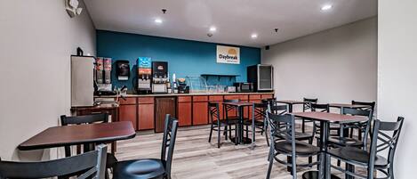 A breakfast area with tables and chairs, a counter with a coffee machine, and a sign for Daybreak Breakfast.