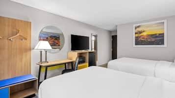 A hotel room with two beds, a desk with a chair, a TV, and a painting of a sunset.