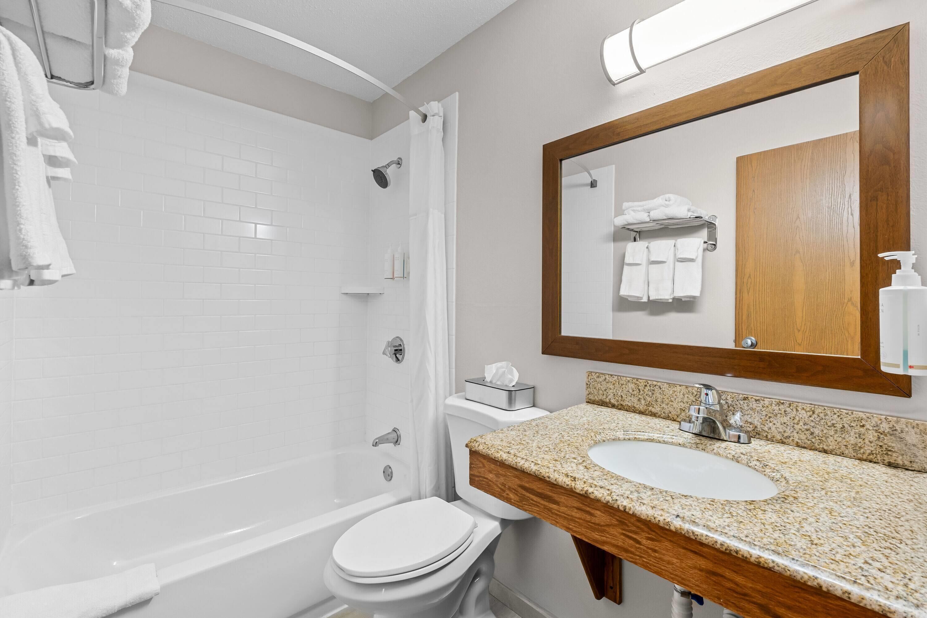 A modern bathroom with a white bathtub, a sink with a wooden countertop, and a large mirror with a wooden frame.