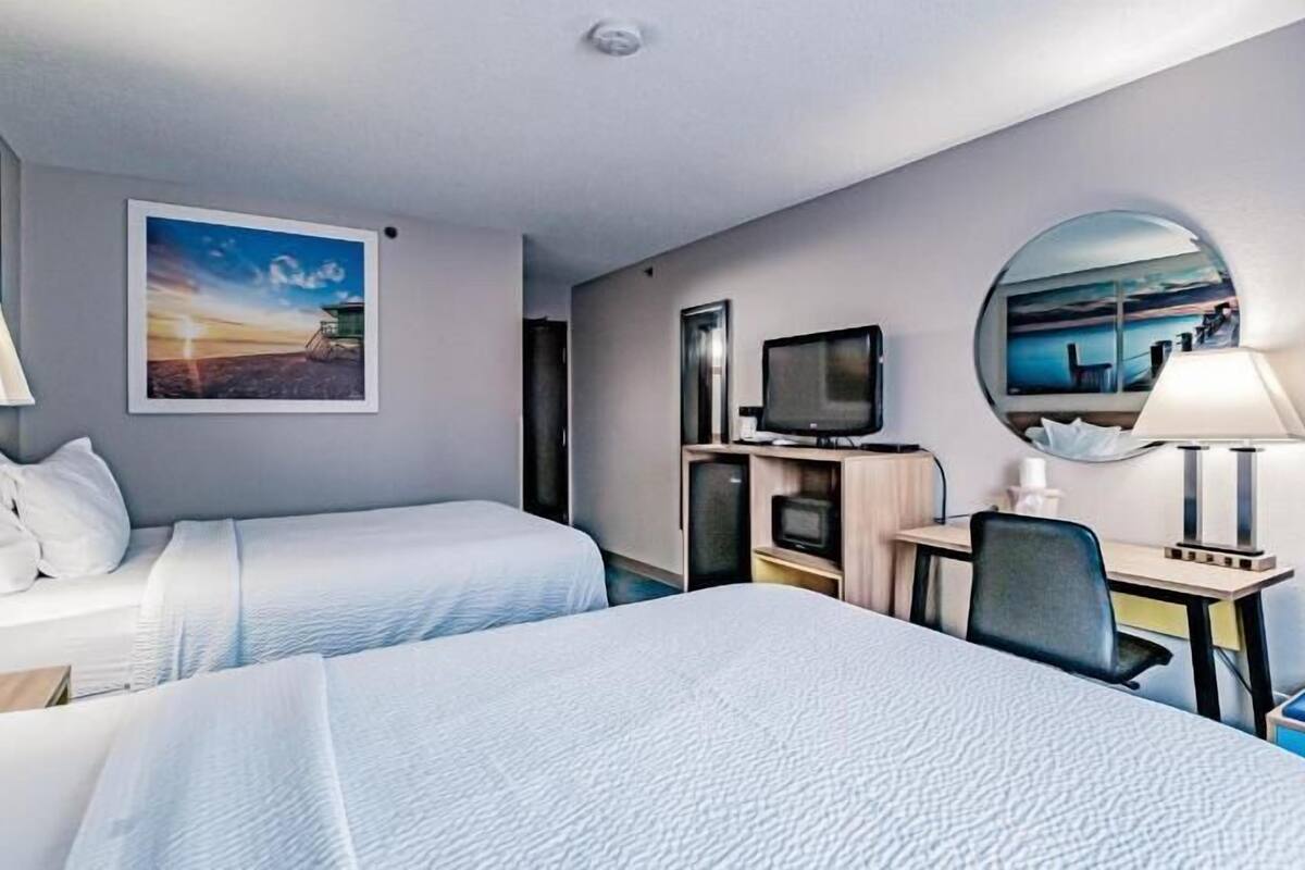 A hotel room with two beds, a desk with a computer, a television, and a mirror.