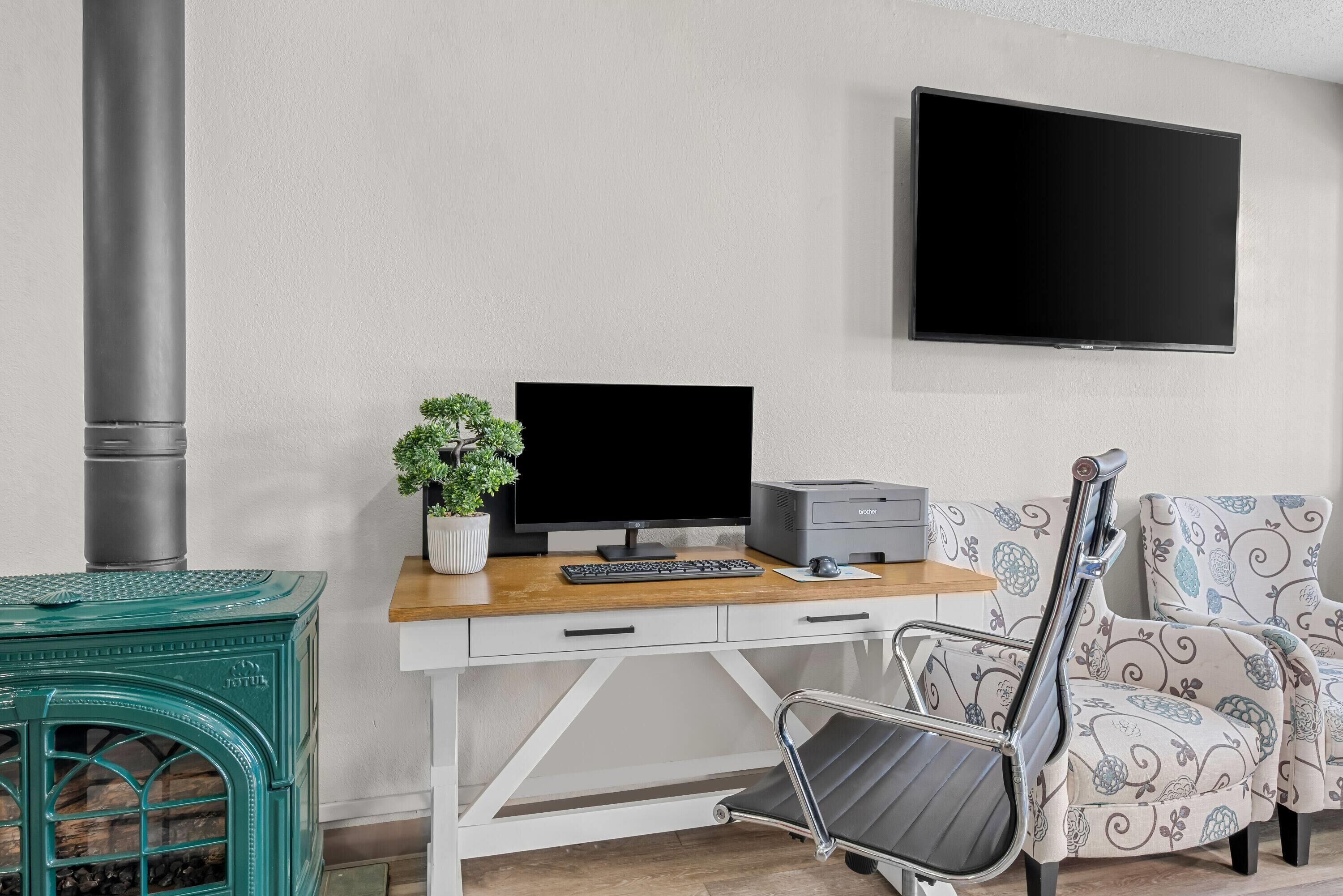 Un salon moderne avec un bureau en bois, un ordinateur, une imprimante, un téléviseur, un canapé et un poêle vert.