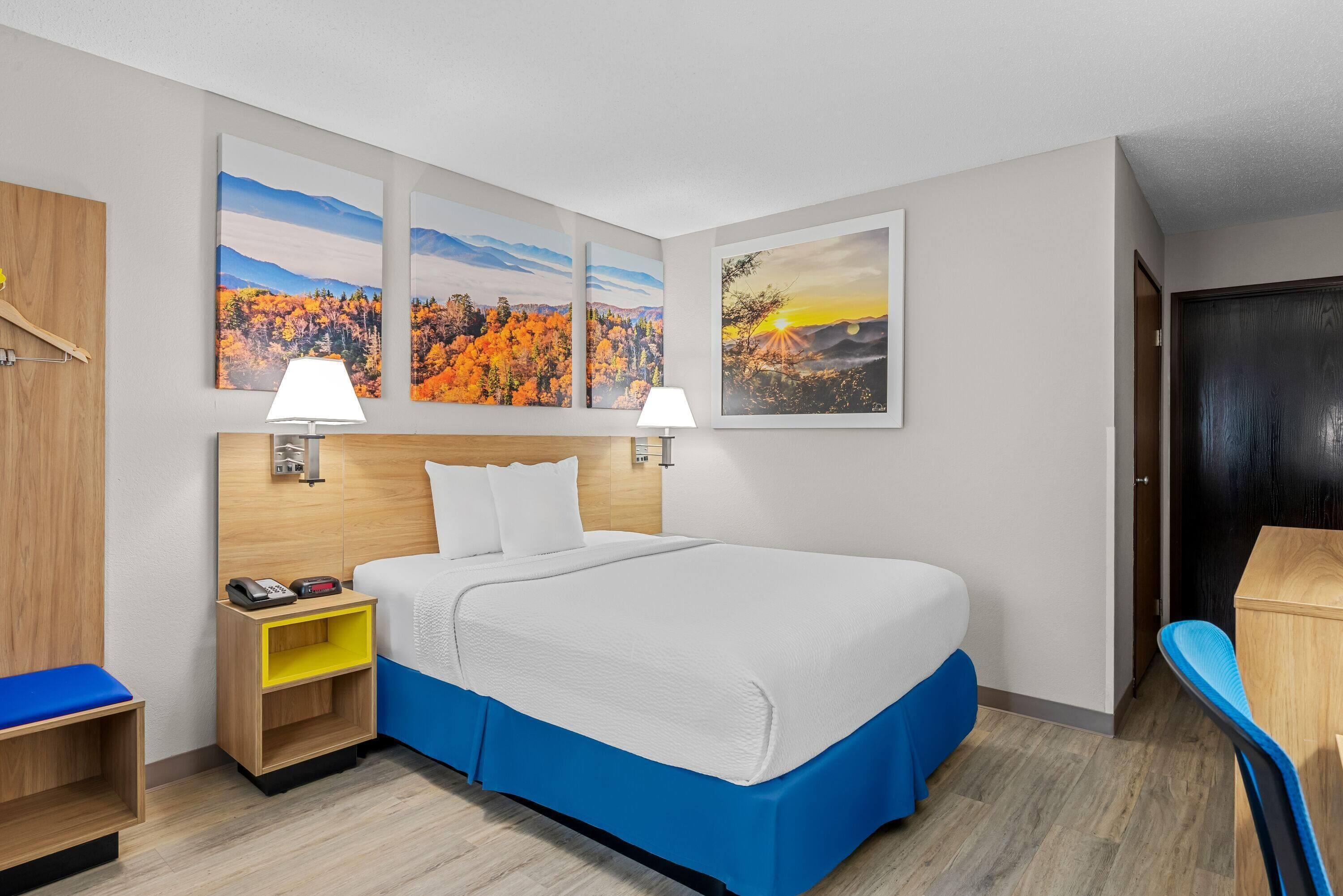 A hotel room with a bed, nightstands, a desk, and wall art.