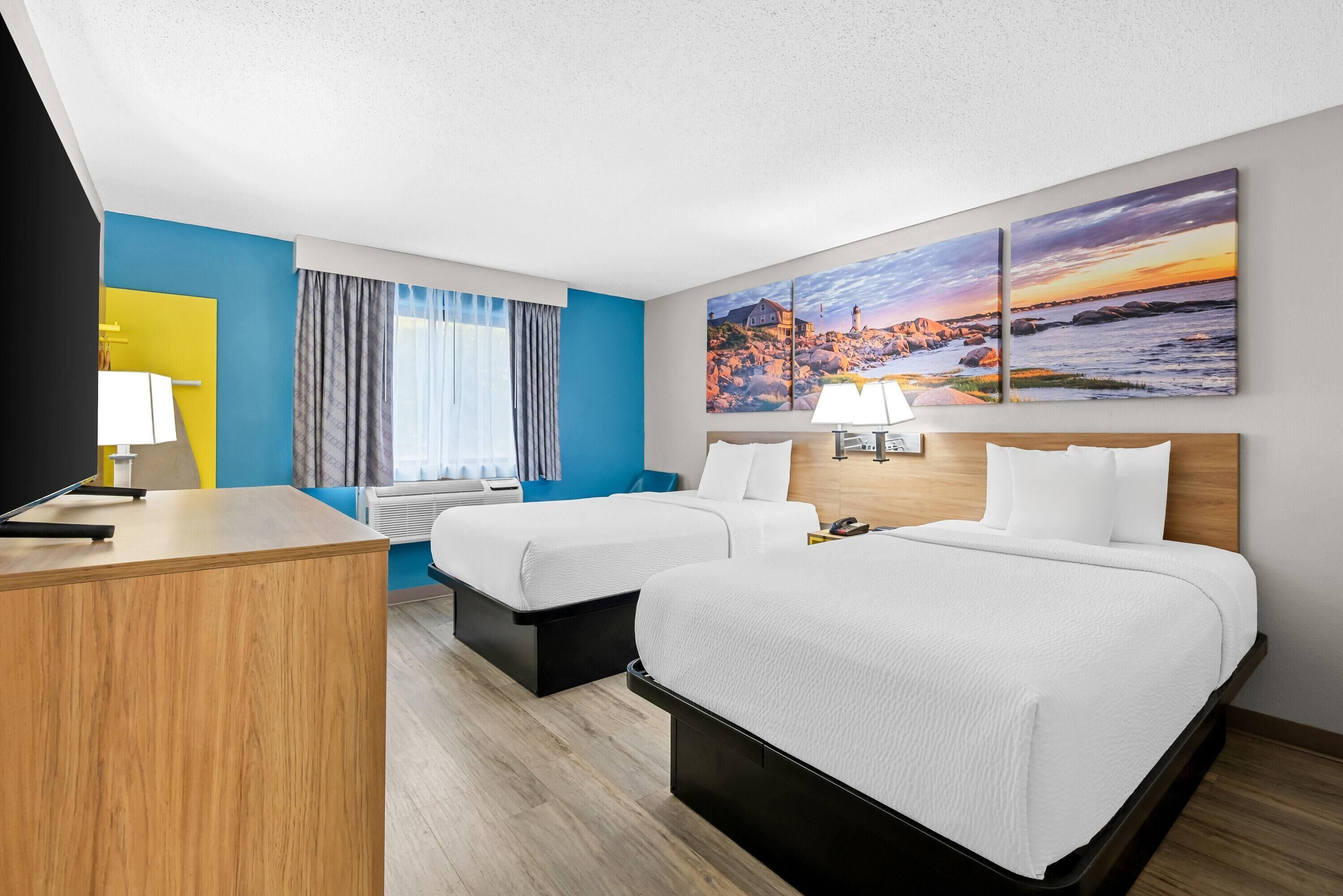 A hotel room with two beds, a desk, a TV, and artwork on the walls.