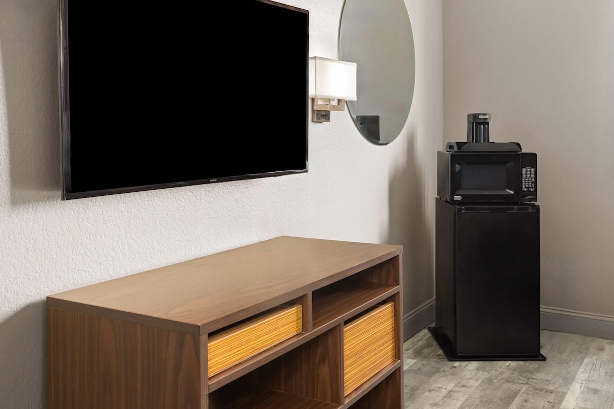 A room with a flat-screen TV mounted on the wall, a small black refrigerator, and a wooden cabinet with drawers.