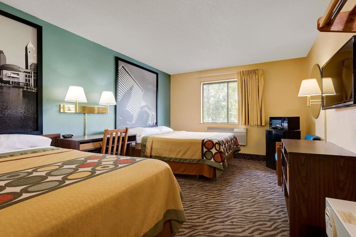 A hotel room with two beds, a desk, a chair, a television, and a window with curtains.