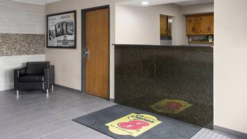 A reception area with a wooden door, a black leather chair, a reception desk, and a kitchen area in the background.