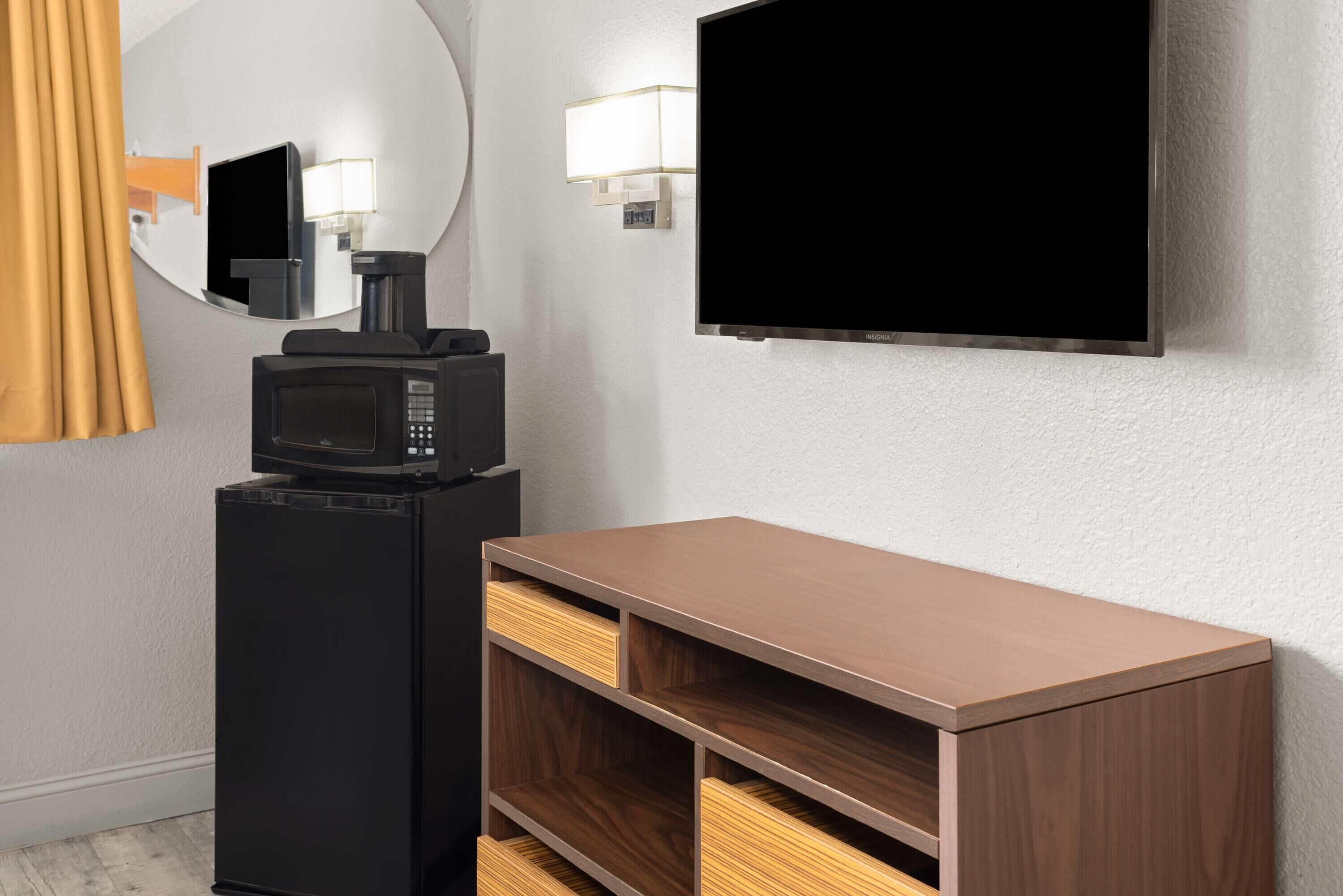 Una stanza con una TV a schermo piatto fissata al muro, un forno a microonde su un mobile nero e un armadio in legno con cassetti.