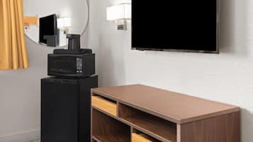 Una stanza con una TV a schermo piatto fissata al muro, un forno a microonde su un mobile nero e un armadio in legno con cassetti.