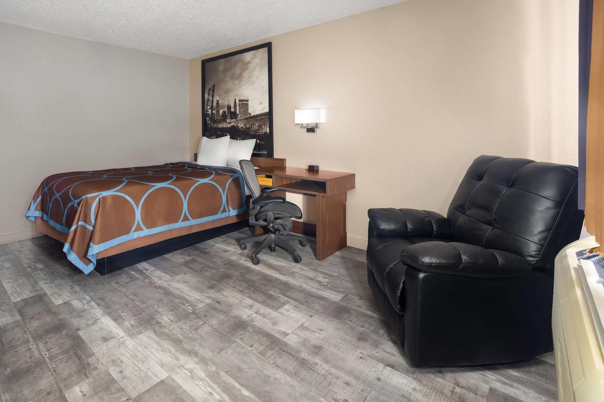 A hotel room with a bed, a desk, a chair, and a cityscape painting on the wall.