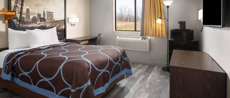 Habitación de hotel con cama, escritorio, equipo de aire acondicionado, lámpara y un cuadro de paisaje urbano.