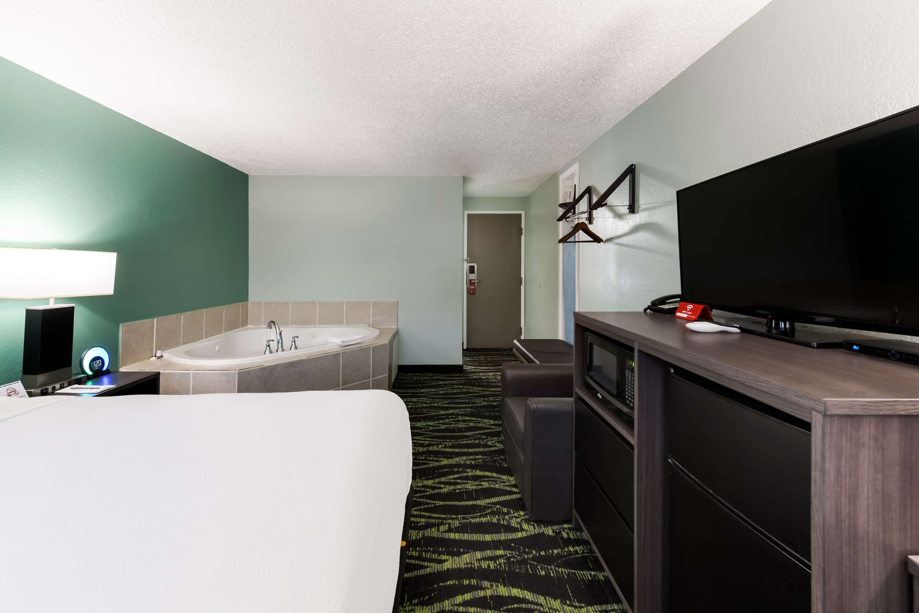 A hotel room with a large bed, a bathtub, a television, and a desk with a computer.