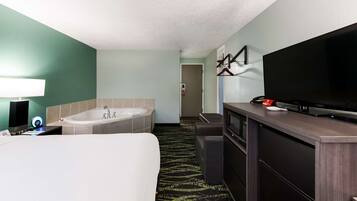 A hotel room with a large bed, a bathtub, a television, and a desk with a computer.