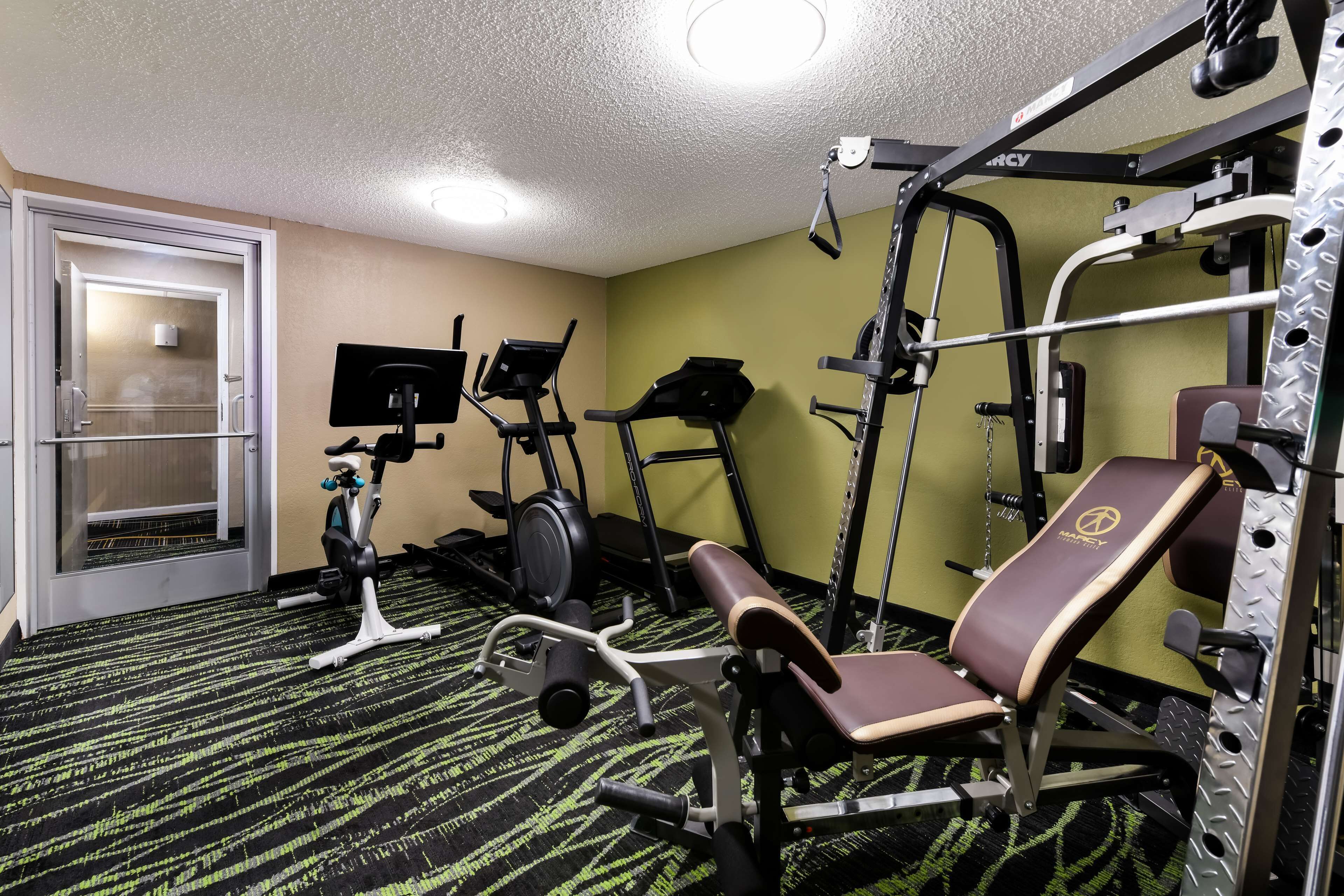 Et fitnesscenter med træningsudstyr, herunder bænkpres, elliptisk træner og motionscykel.
