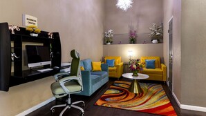 Una sala de estar moderna con un sofá azul, sillones amarillos, un escritorio con una computadora y una alfombra colorida.