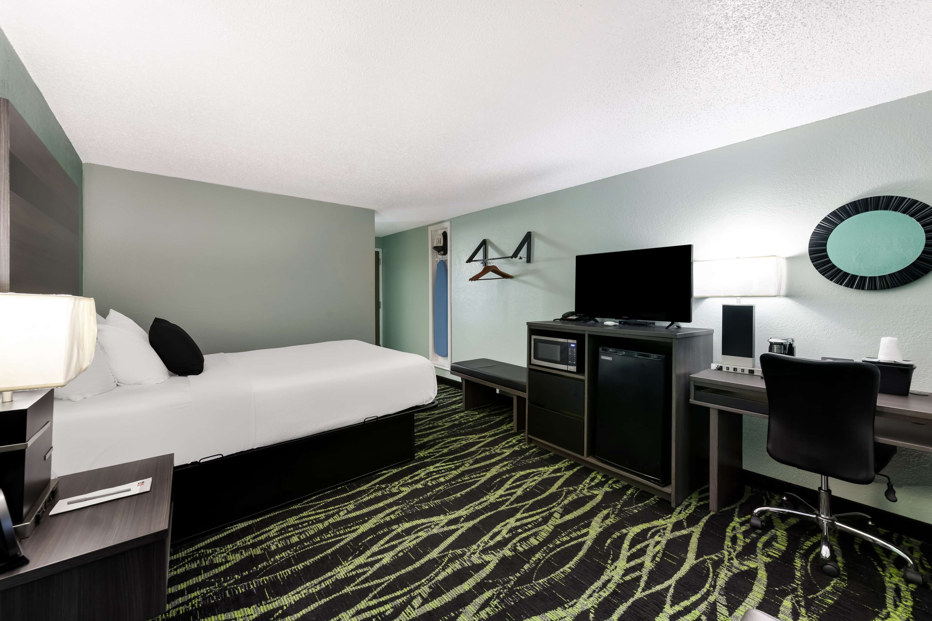 A hotel room with a bed, desk, chair, TV, and a microwave.