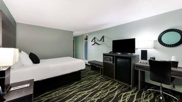 A hotel room with a bed, desk, chair, TV, and a microwave.