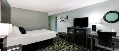 A hotel room with a bed, desk, chair, TV, and a microwave.