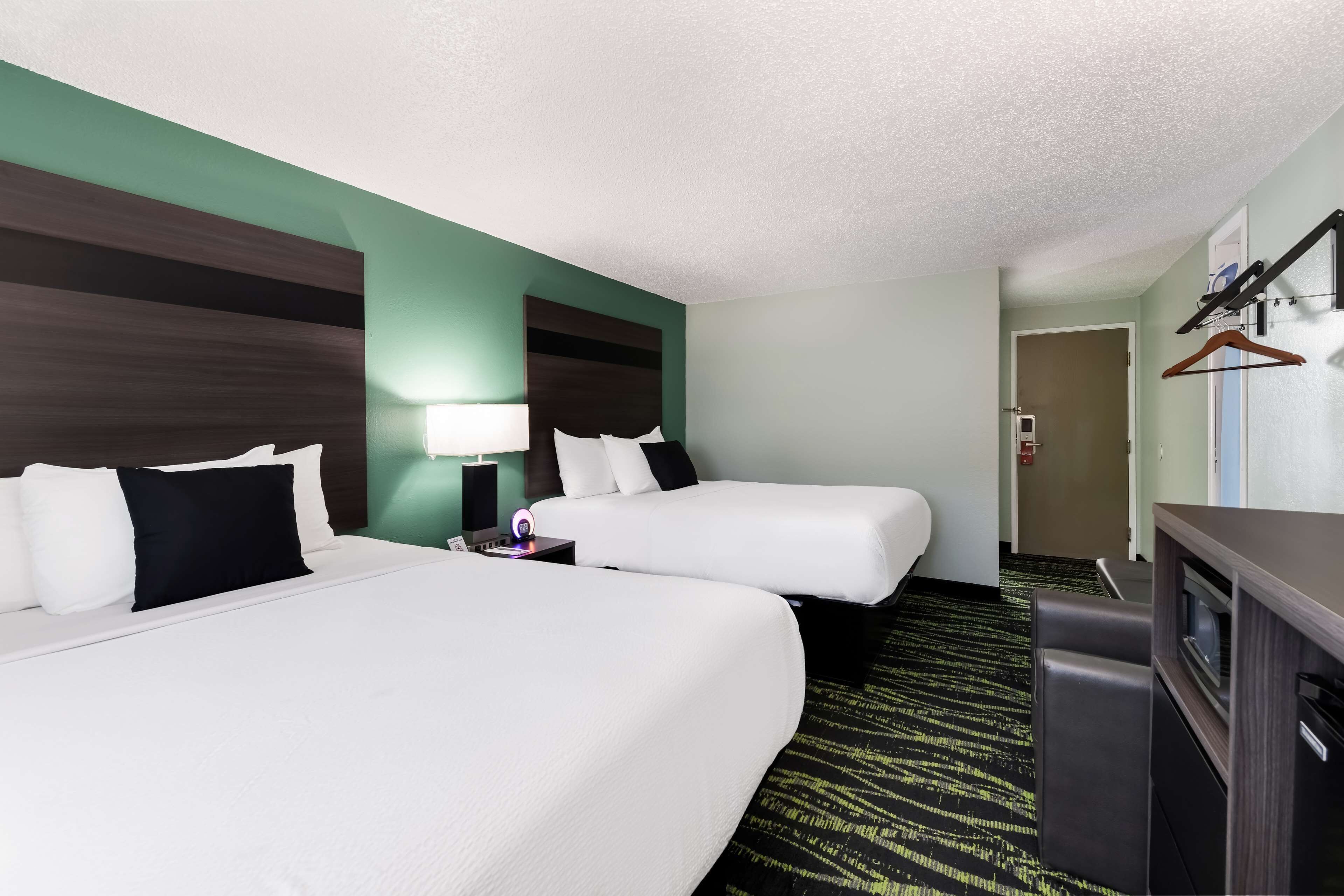 A hotel room with two beds, a desk, a dresser, and a coat rack.