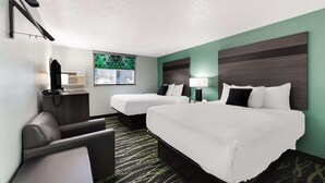 Una habitación de hotel con dos camas, un escritorio con lámpara, una silla y un televisor.