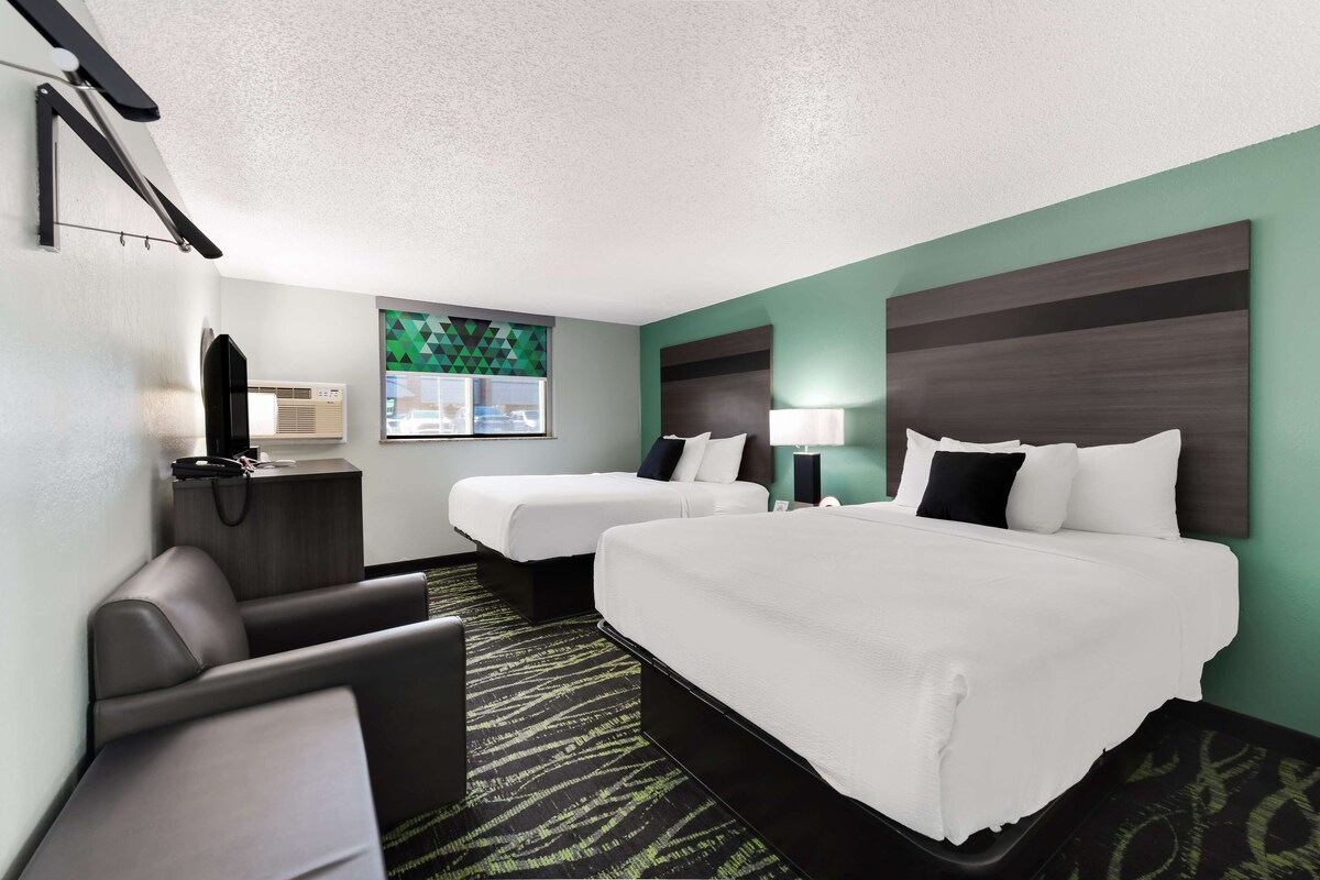 A hotel room with two beds, a desk with a lamp, a chair, and a TV.