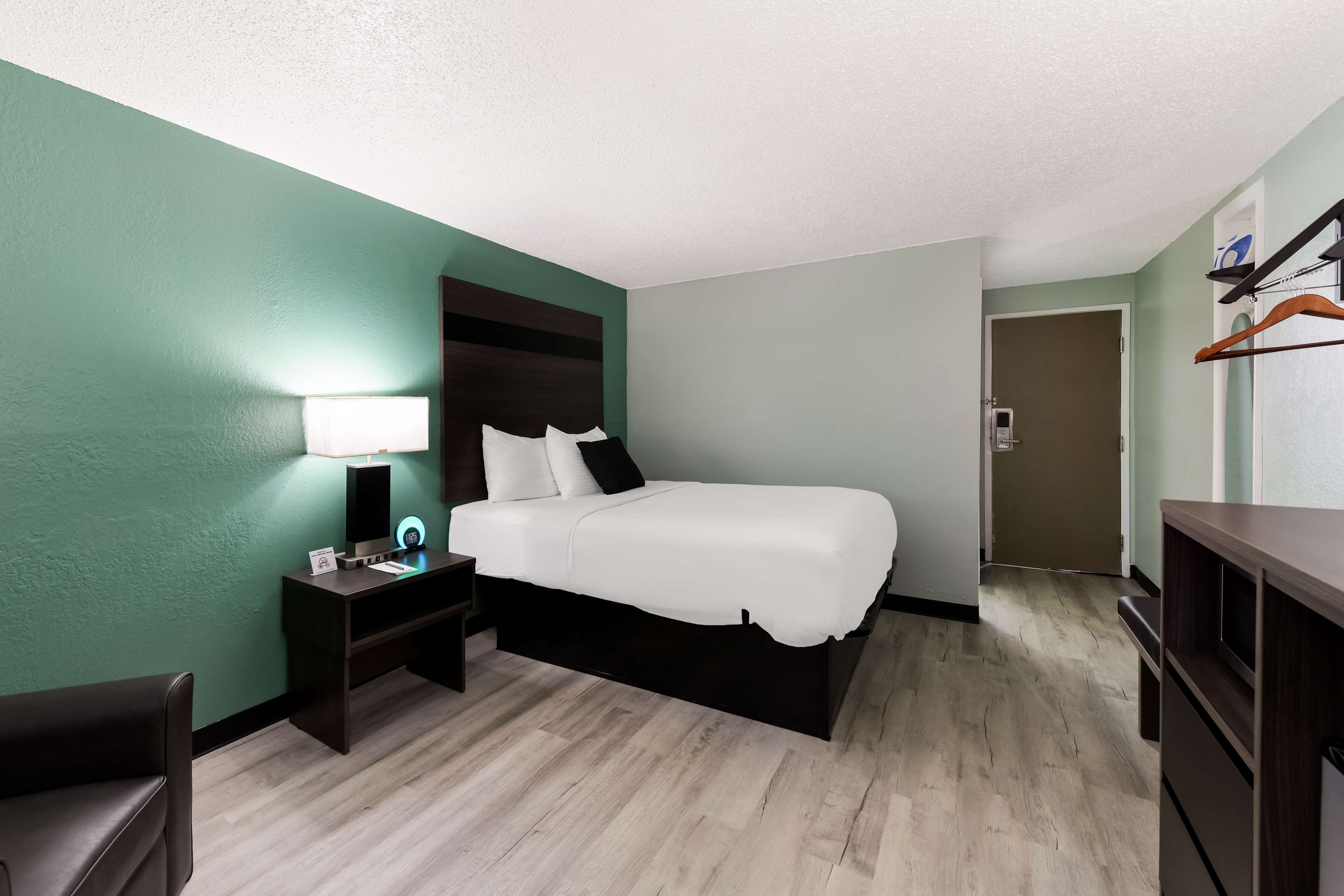 Una habitación de hotel con una cama, un escritorio con lámpara, una silla y un armario.