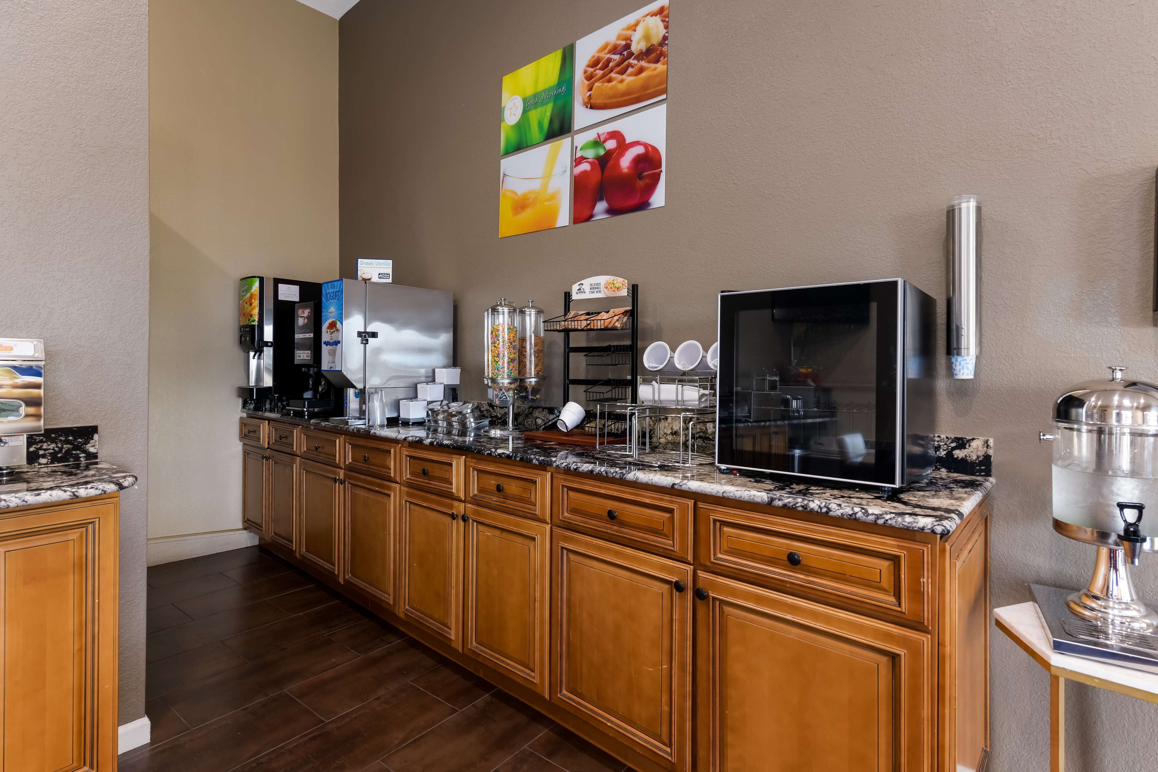A hotel kitchen with a marble countertop, wooden cabinets, a coffee station, a refrigerator, a microwave, and a water dispenser.