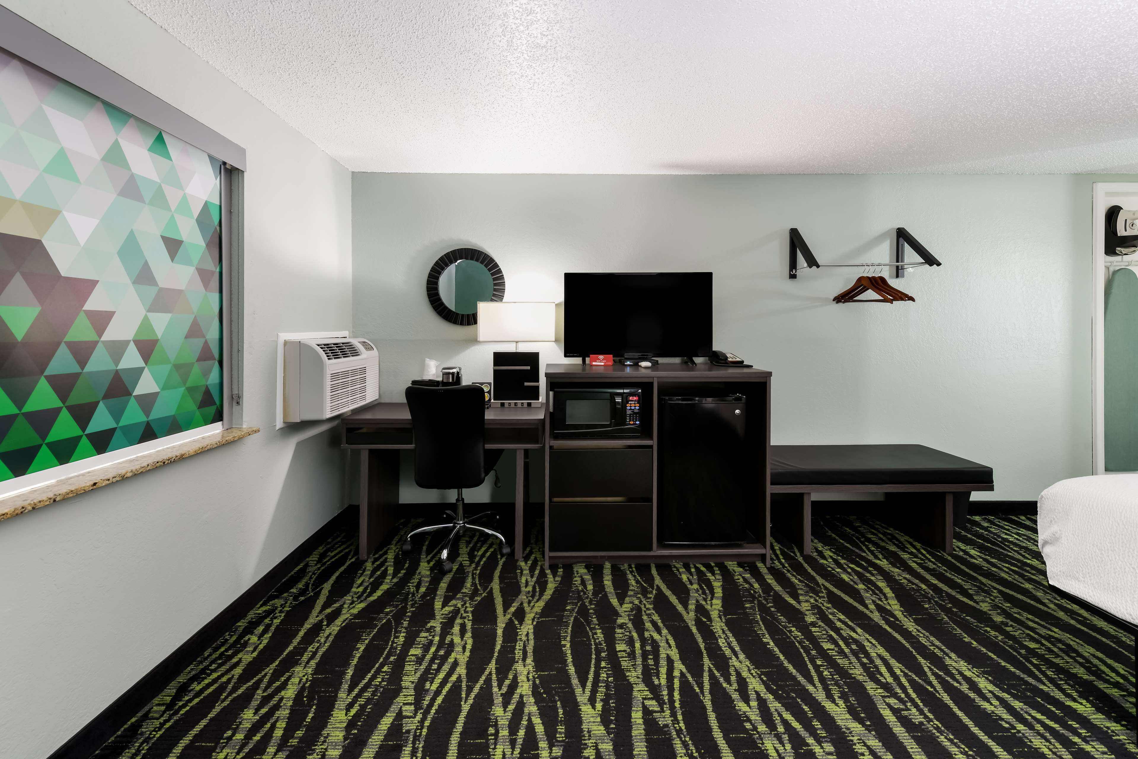 A hotel room with a desk, a television, a microwave, a mini-fridge, a bed, and a bathroom with a towel rack.