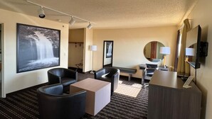 Habitación de hotel con una televisión de pantalla plana grande, un sofá, una mesa de centro, un escritorio y un espejo.