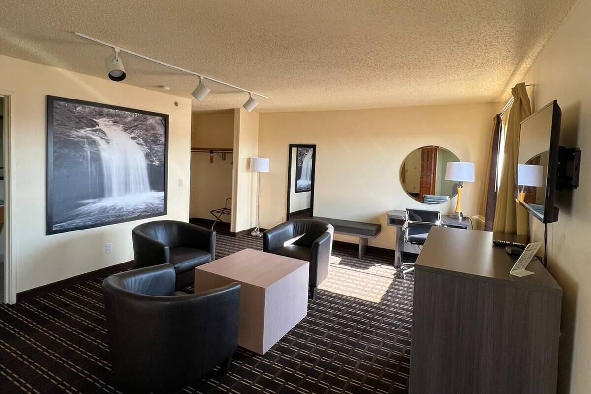 A hotel room with a large flat-screen TV, a sofa, a coffee table, a desk, and a mirror.