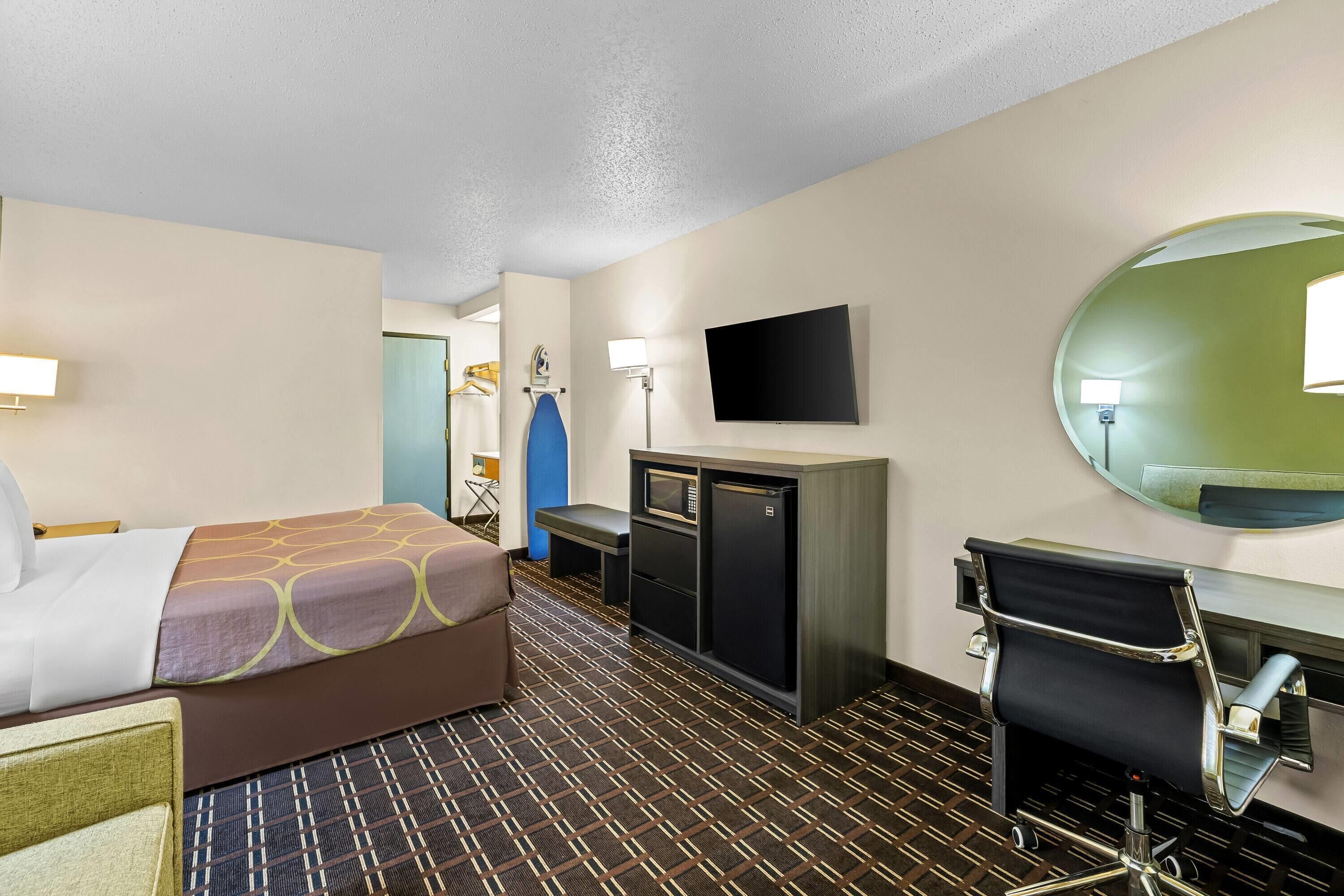 Una habitación de hotel con cama, escritorio, silla, televisor y espejo.
