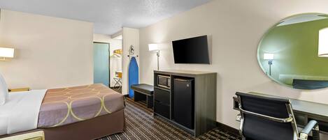 Una habitación de hotel con cama, escritorio, silla, televisor y espejo.