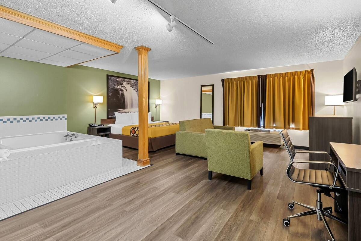A hotel room with a large bathtub, a sofa, a desk, and a chair.