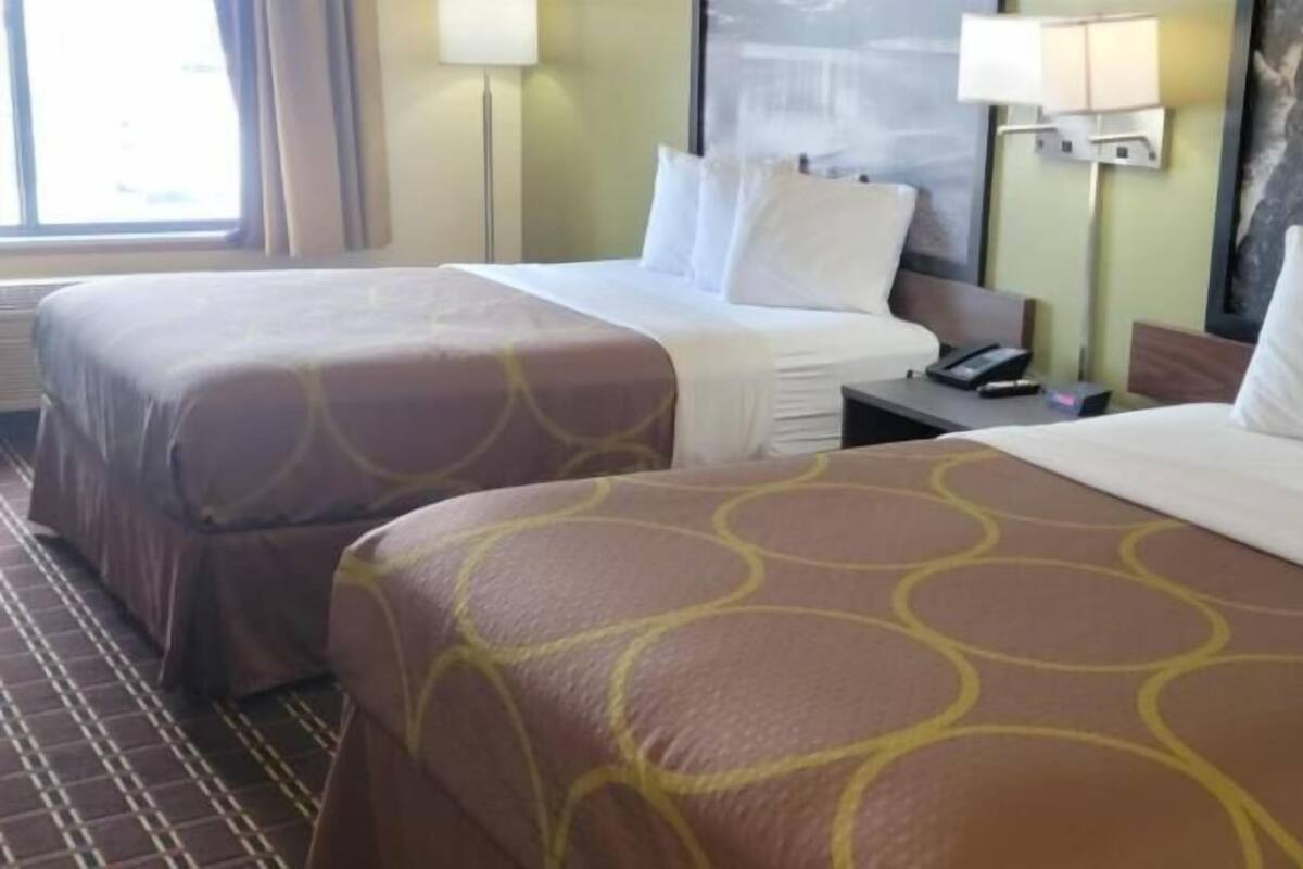 A hotel room with two beds, a nightstand, a lamp, and a window.