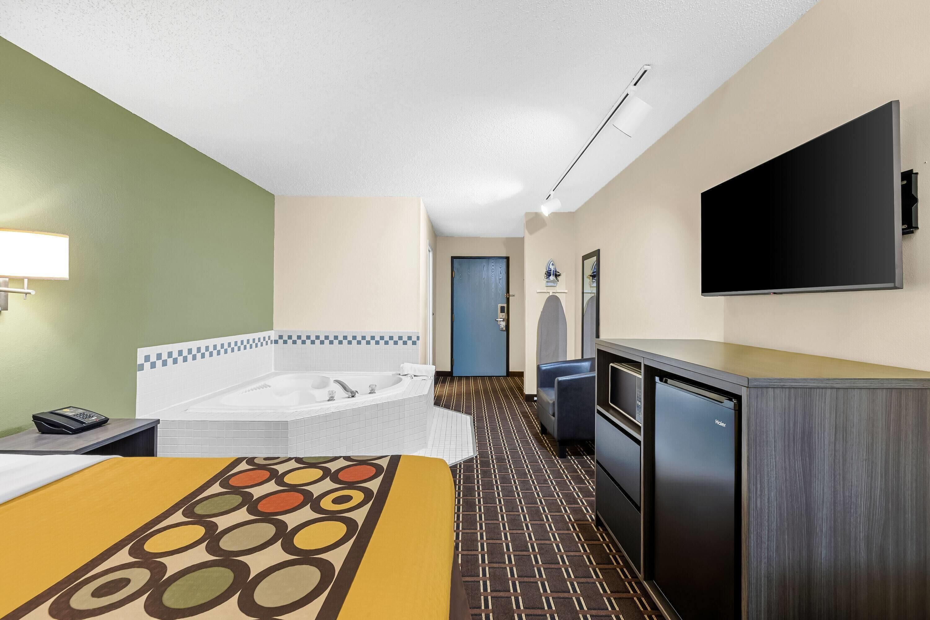 Habitación de hotel con cama, baño con bañera, televisión de pantalla plana y minibar.