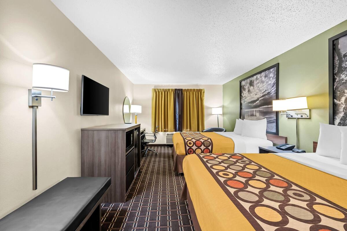 A hotel room with a bed, a desk, a chair, a TV, and a painting on the wall.
