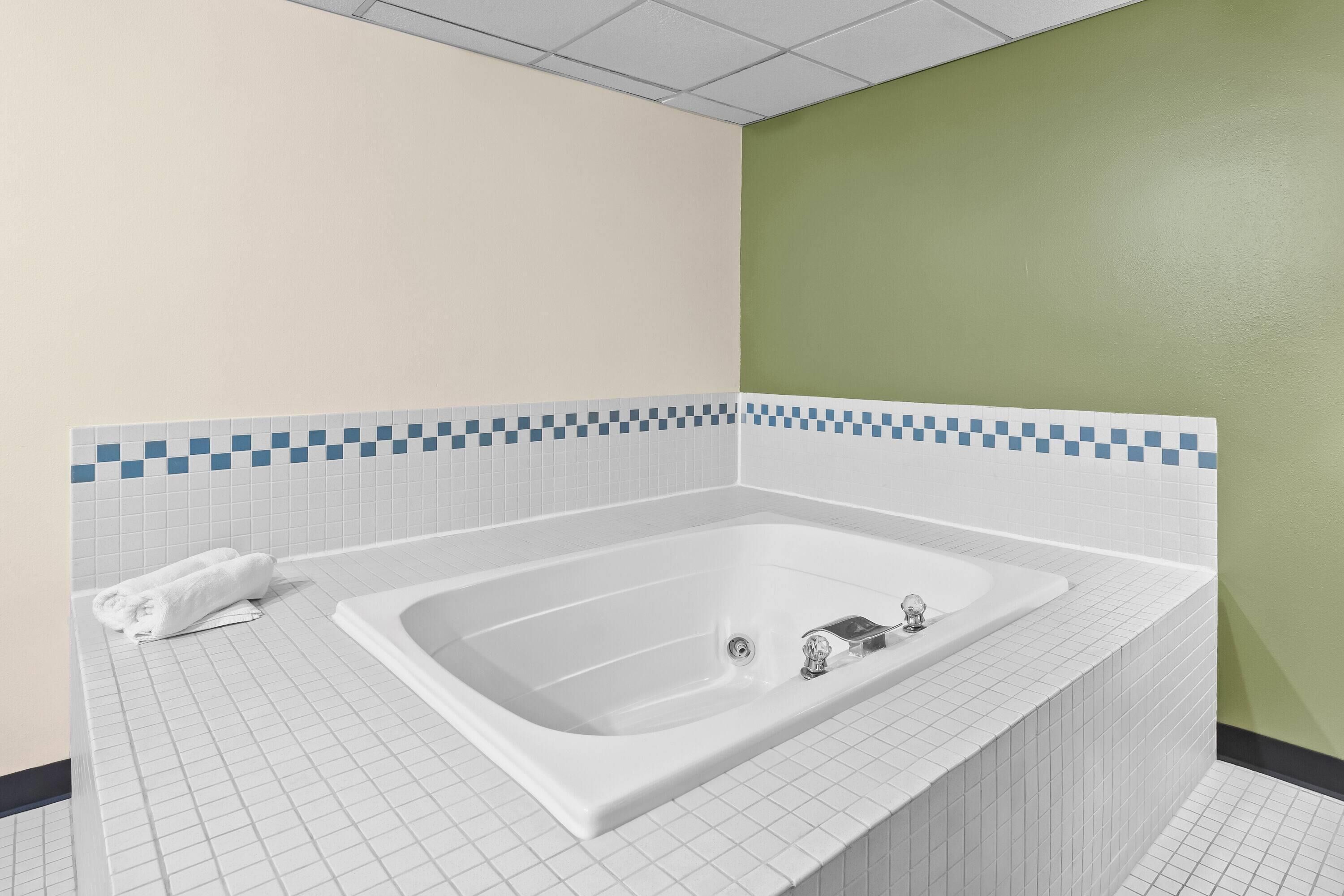 A bathroom with a large bathtub, white tiled walls, and a green accent wall.