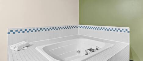 A bathroom with a large bathtub, white tiled walls, and a green accent wall.