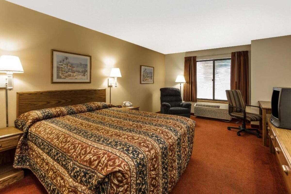 A hotel room with a large bed, two chairs, a desk with a television, and two lamps.
