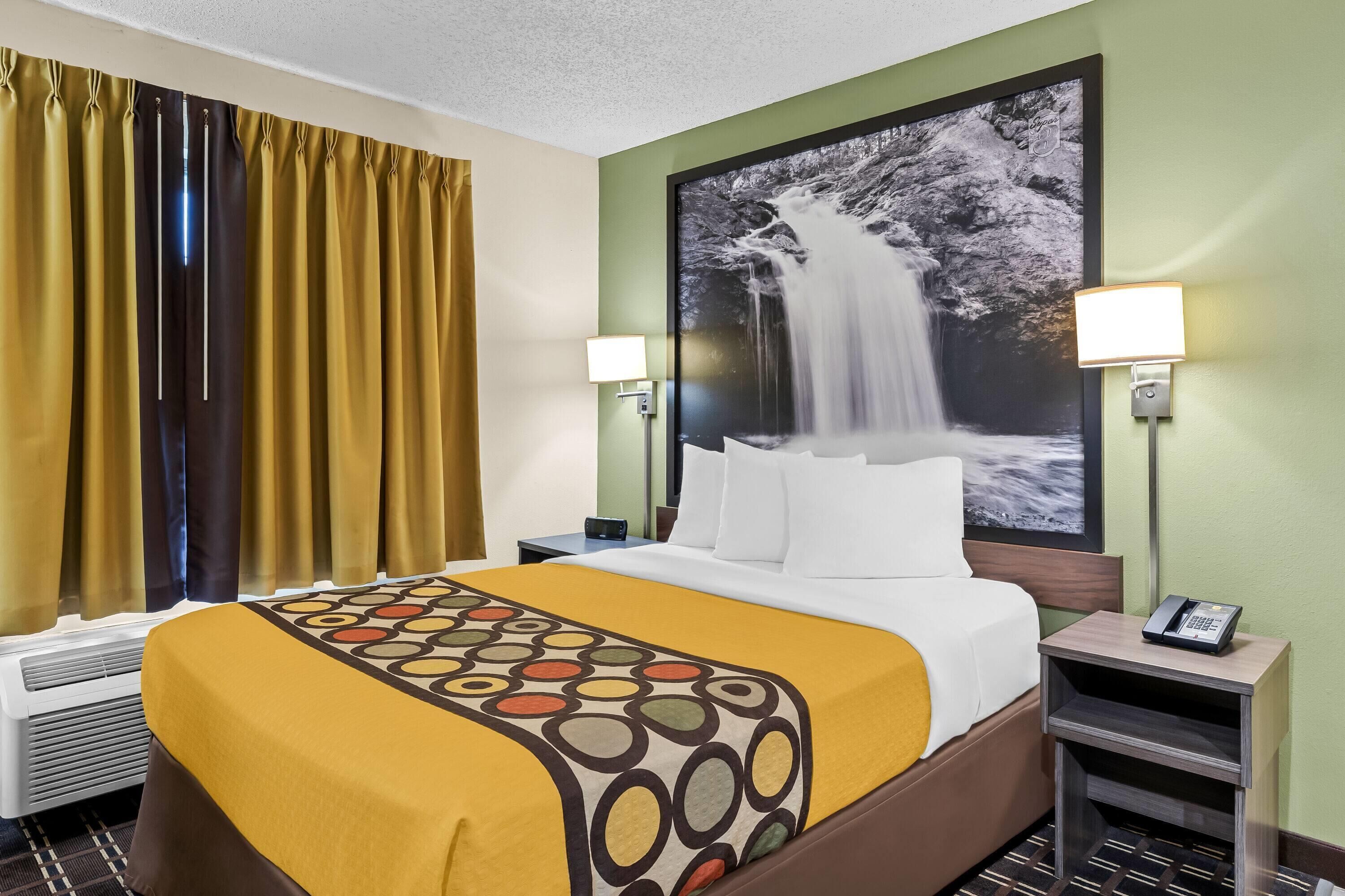 A hotel room with a bed, a nightstand, a telephone, and a wall-mounted picture of a waterfall.