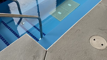A swimming pool with clear blue water, a metal ladder, and a drain cover.