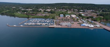 An aerial view of a marina with boats docked, a small building, and a dock extending into the water.